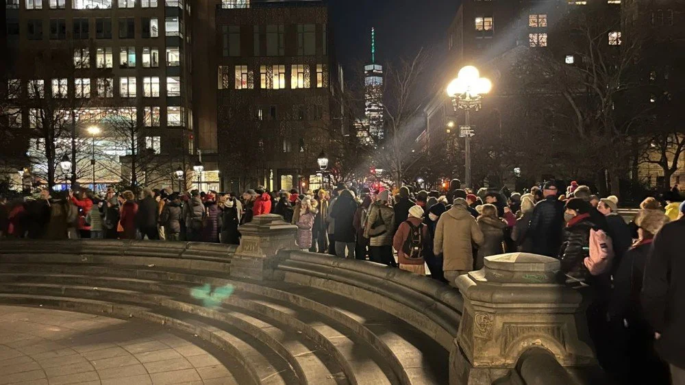 Large crowd gathered in Washington Square Park at night for Unsilent Night, with One World Trade Center visible in the background
