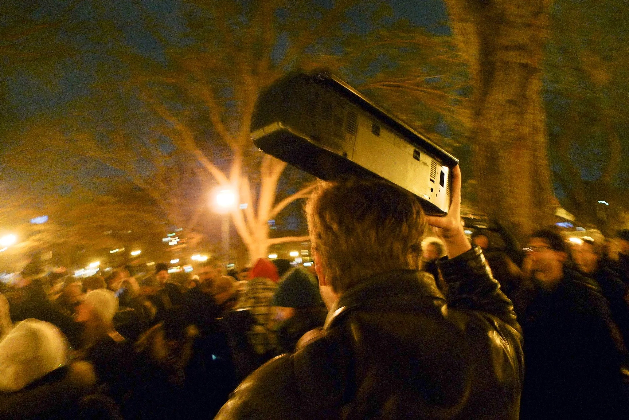 Unsilent Night participant holding a boombox overhead while walking through a crowd at night