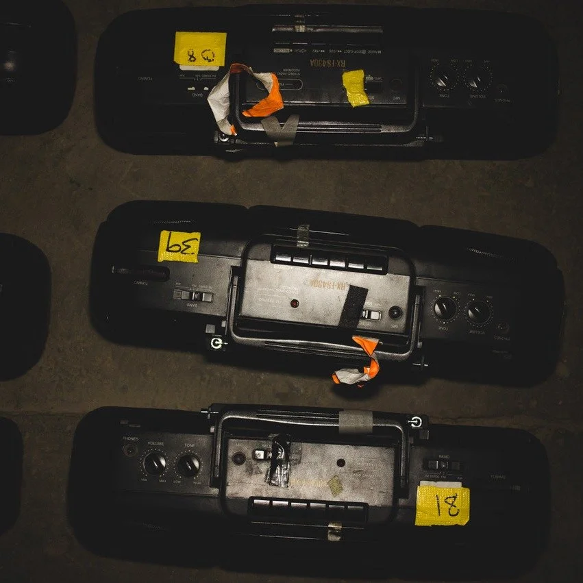 Overhead view of three vintage boomboxes laid out with numbered tags