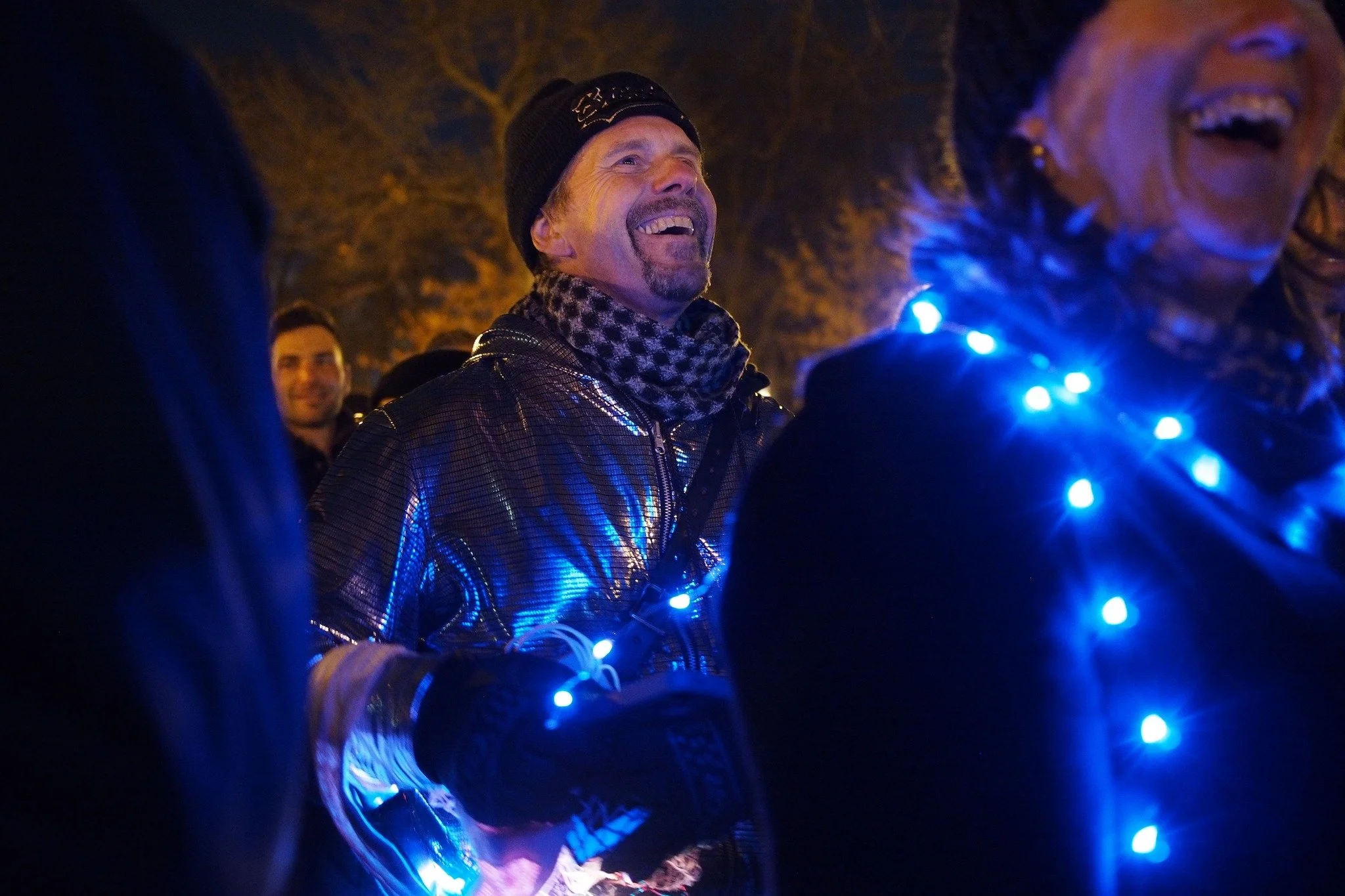 Unsilent Night participants laughing together at night, one wearing a strand of blue lights